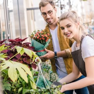 smiling florist and customer standing with plants near flower shop